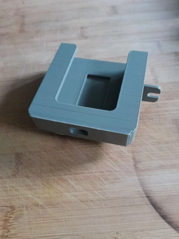 la face avant d'un support pour téléphone imprimé en 3D: il y a une ouverture sur tout l'avant pour pouvoir voir et accéder facilement à l'écran, une petite griffe sur le côté pour suspendre le cable usb, et un trou sur la face inférieure qui permet le passage d'un cable usb pour la charge