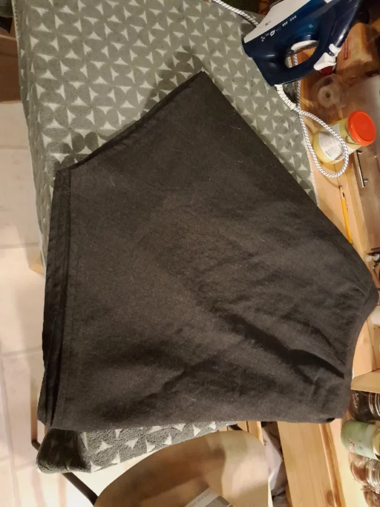 une jupe grise en lainage,  pointue en son milieu, avec des pinces à la taille,  disposée à la va vite sur une table à manger