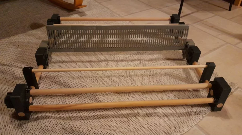 Vue du même métier de plus près, de face et un peu de dessus : on peut voir les deux molettes à gauche pour enrouler et dérouler à l'arrière et à l'avant du métier, et deux supports doubles pour les cadres, histoire de voir venir