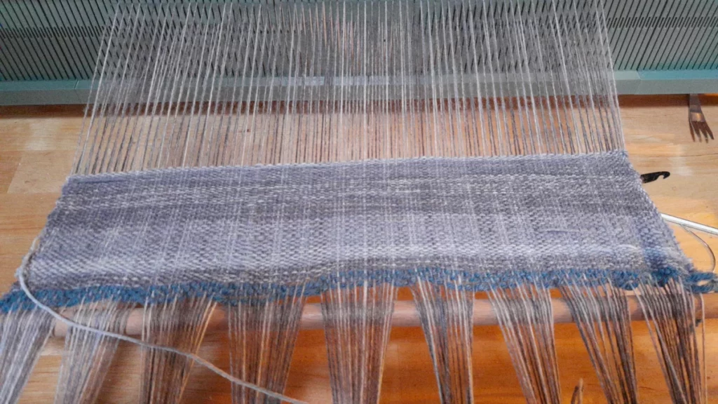 les dix premiers centimètres d'écharpe laissent voir une longue variation de teines de gris: une petite section suivie parprès de la moitié dans une teinte médiane, puis une teinte plus foncée. les variations de la chaîne laissent apparaître un discret quadriage aléatoire dans les mêmes tons. les bords se resserrent un peu trop vers le centre.