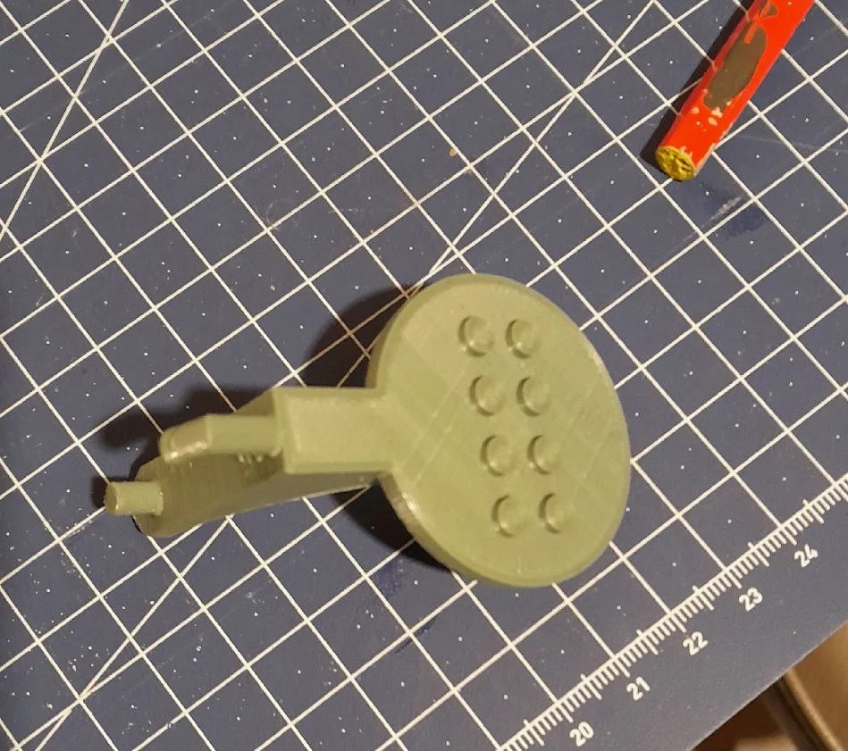 Le support vu de dessus sur la planche de découpe. On voit les huit pegs d'accroche au modèle lego sur le disque, puis deux crochets à l'arrière de l'équerre ,pour la suspension sur le pegboard skadis