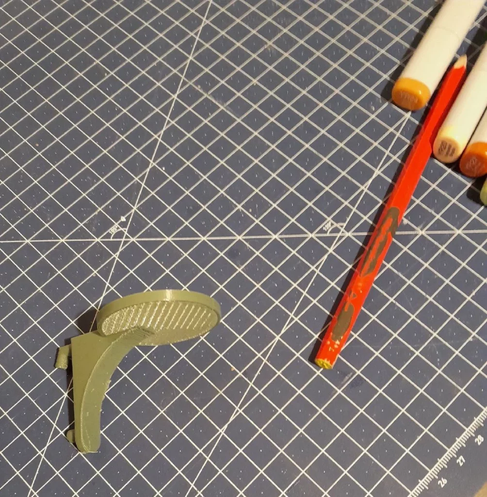 le support est tout seul sur une planche à découper, à côté d'un crayon pour l'échelle. C'est un disque sur une équerre au profil arqué. Il rappelle un peu le vaisseau Enterprise.