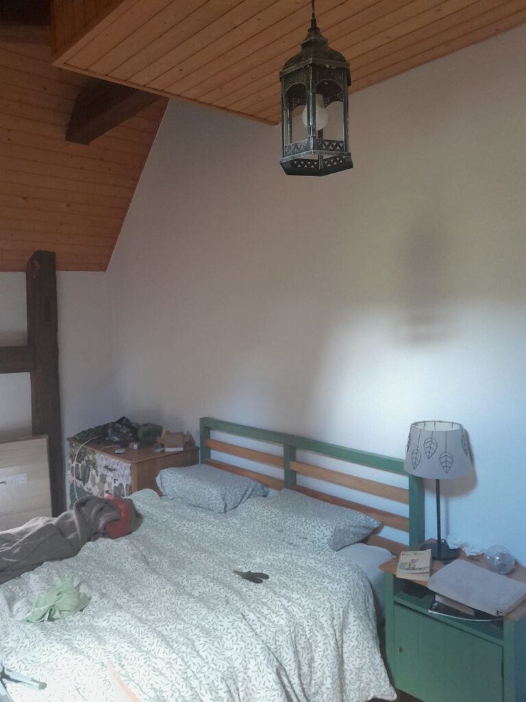 une suspension en forme de lanterne trône dans une chambre rustique aux poutres apparentes. Elle semble fabriquée en fer forgé dont elle a en tout cas le rendu très noir et l'aspect de robustesse et de rudesse, et est ornementée de petits jours géométriques sur tout son pourtour et en décoration des arches qui entourent les vitres de la lanterne, projetant des petits motifs lumineux lorsqu'elle est allumé.