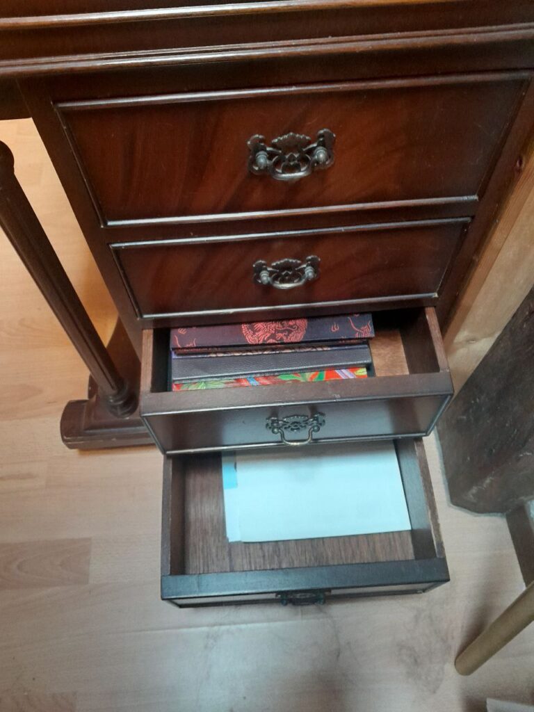les deux derniers tiroirs du flanc droit du Davenport sont ouverts, laissant voir dans le premier une raisonnable pile de carnets lignés A5 aux jolies couvertures ouvragées, et dans le second, du papier à lettres neutre