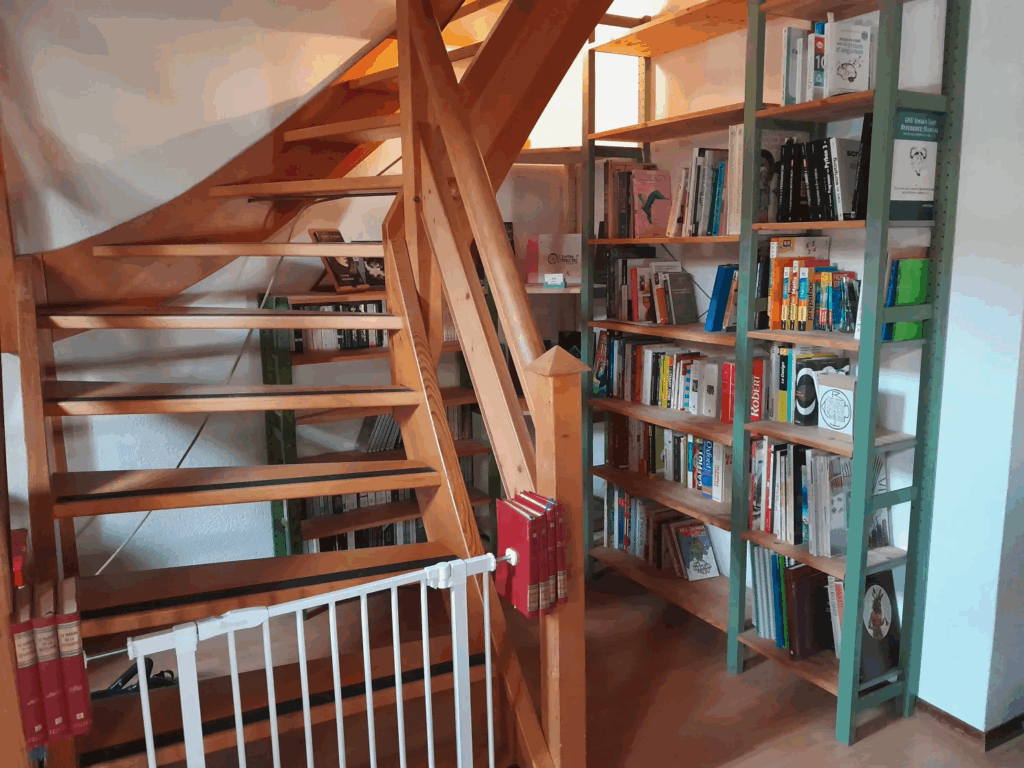 vue du coin bibliothèque depuis devant l'escalier : les bibliothèques forment effectivement un angle contre le mur sur lequel est adossé l'escalier, laissant un bon mettre de passage à côté de l'escalier et une petite niche dessous, dans laquelle on peut facilement entreposer un pouf, un petit fauteuil de sol ou un matelas