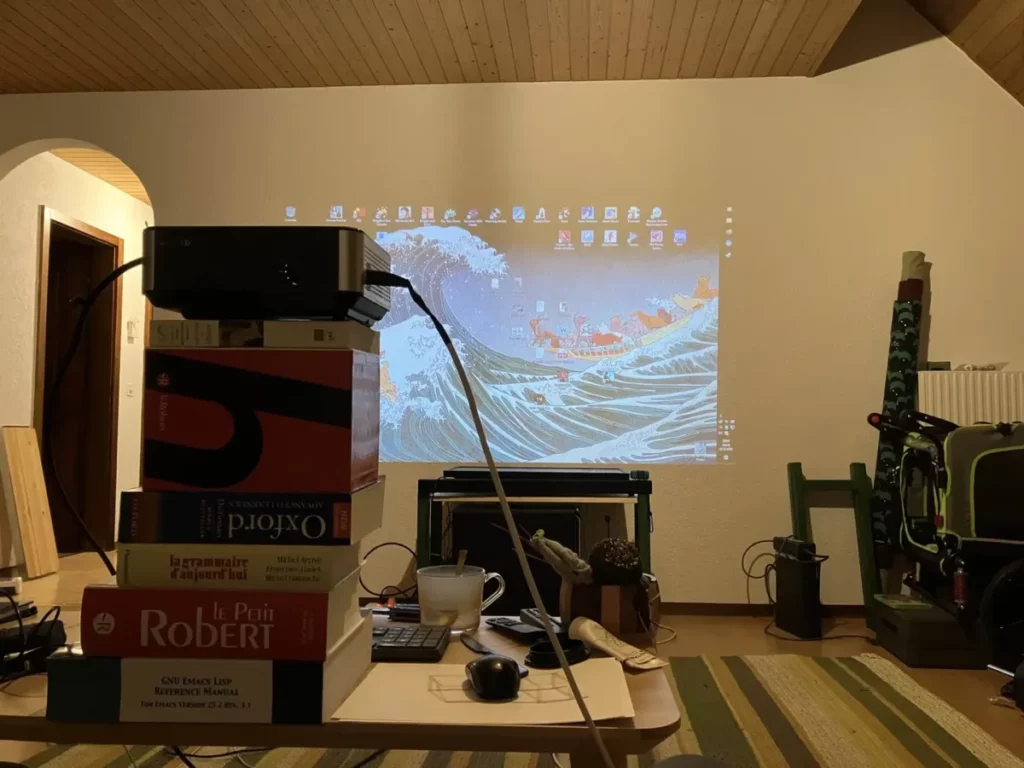 Une pile de dicos soutiennent un projecteur qui projettent mon bureau du PC du salon