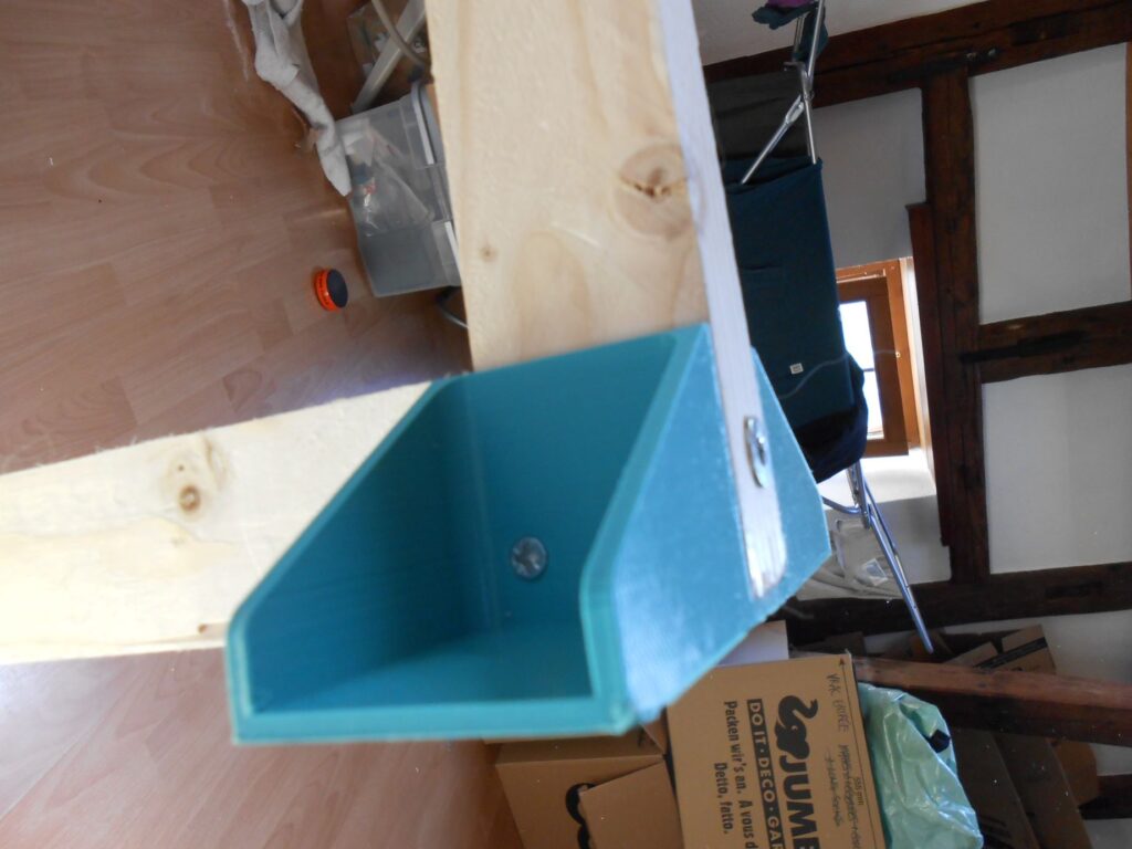 un pied-équerre vu de 3/4 dans l'autre sens, avec une vis en bas à gauche. On voit bien qu'il est inséré autour du cadre en bois et qu'il s'y enchasse parfaitement. 