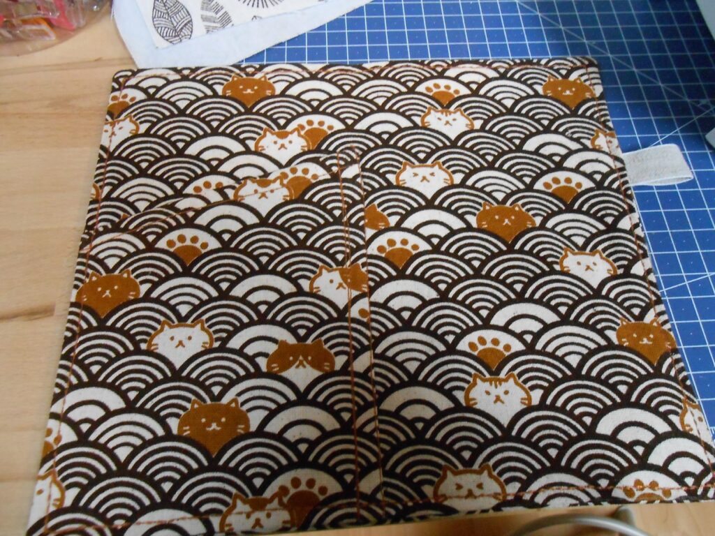 la couverture est assemblée. C'est un rectangle de tissu dont sort une boucle sur le côté droit, et où se trouve une poche sur le côté gauche.