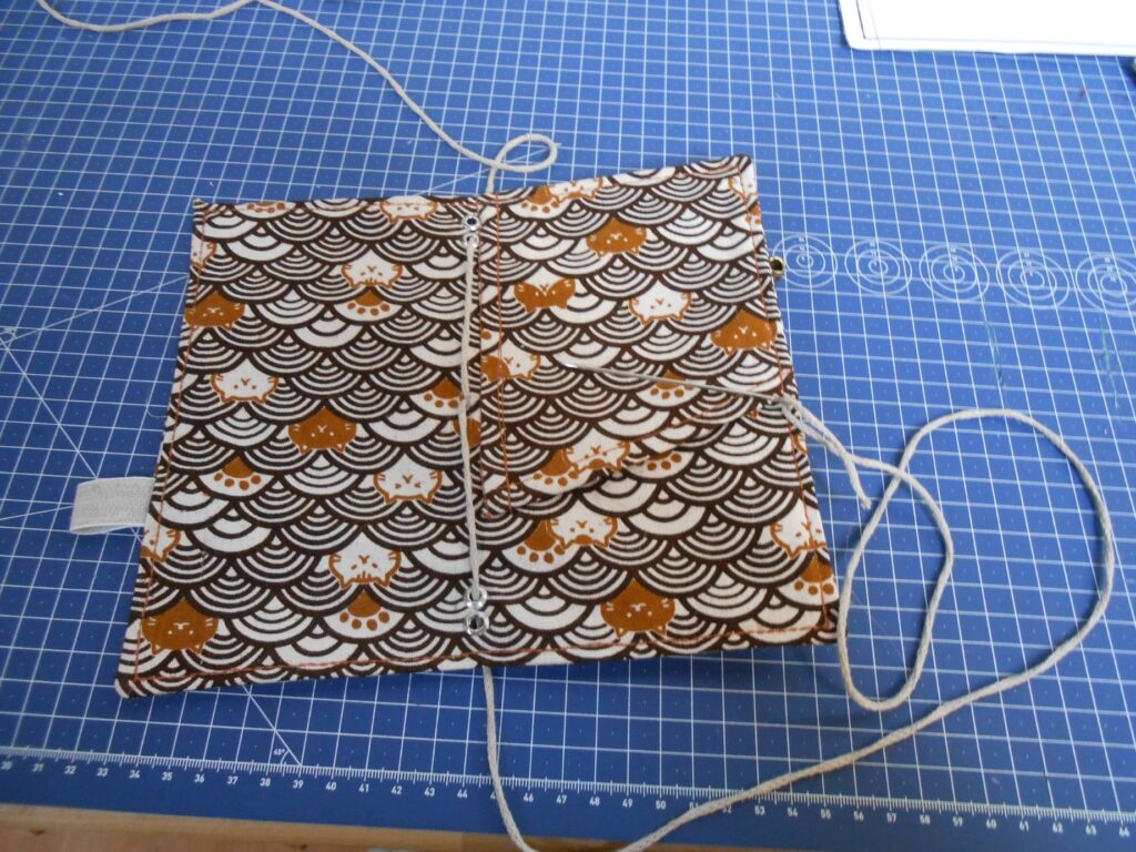 Les deux brins s'écartent au centre de l'intérieur de la pochette. Ils passent respectivement dans les premiers trous du haut et du bas de la couverture.