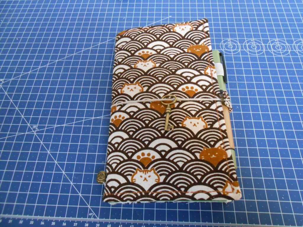 la pochette fermée. La cordelette passe tout autour de la pochette, enveloppant le stylo plume au passage.