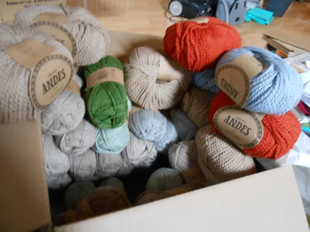 Un carton bourré de pelotes de laine jusqu'à la gueule : de la bulky en bleu ciel, rouille et camel, et une TONNE d'aran, en vert vif avec pas mal de jaune dedans, vert d'eau, beige clair, beige chiné et gris clair