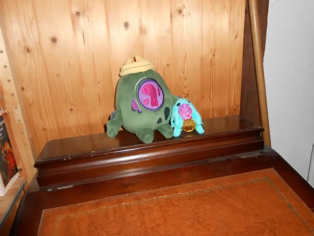 posé sur un secrétaire, la grande peluche greed protège sous son tentacule son nouveu petit frère, la petite peluche greed de l'anniversaire des dix ans