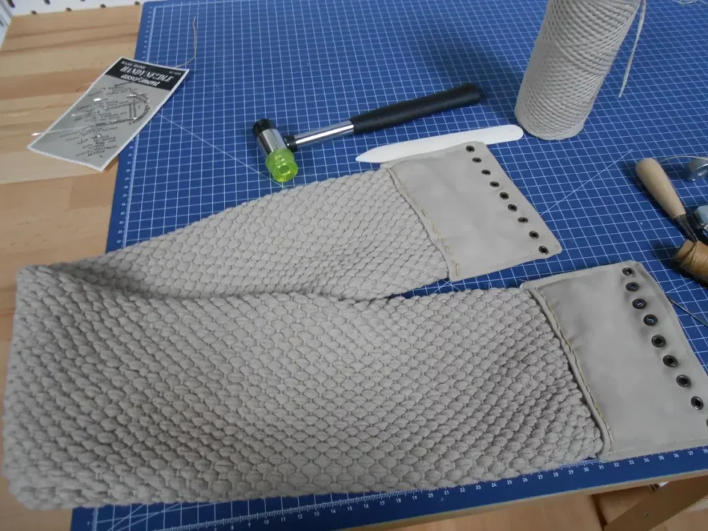 la ceinture en question pliée sur une planche de découpe. Tons "nature" pour le coton (un beige clair) et faux cuir assorti, fil ciré caramel et oeillets laiton.